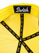 Close-up of the back of a bright yellow Swish brand baseball cap, showing the black interior strap system with yellow Swish text and a black brand patch on the crown.